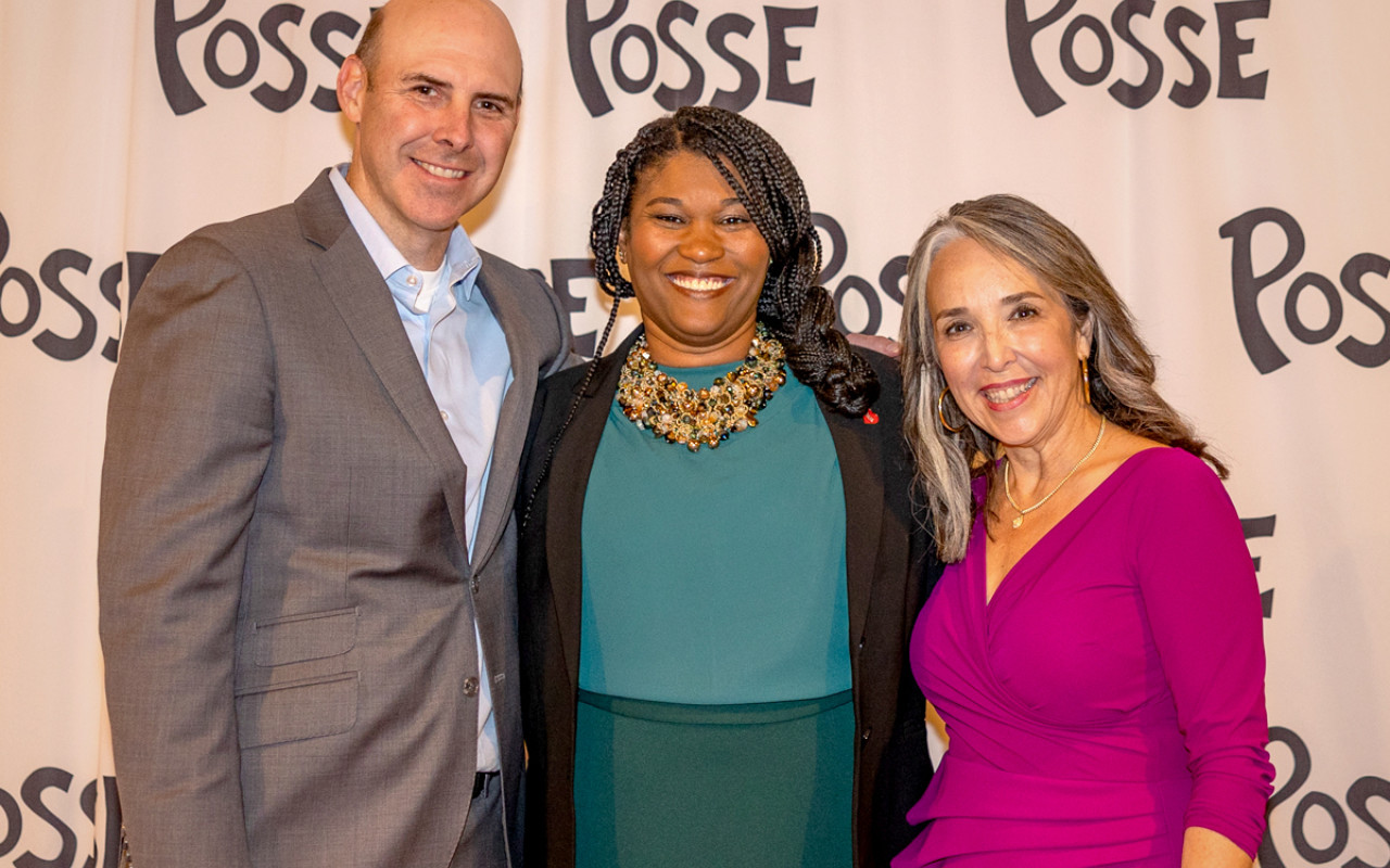 Three people smiling in front of a step and repeat